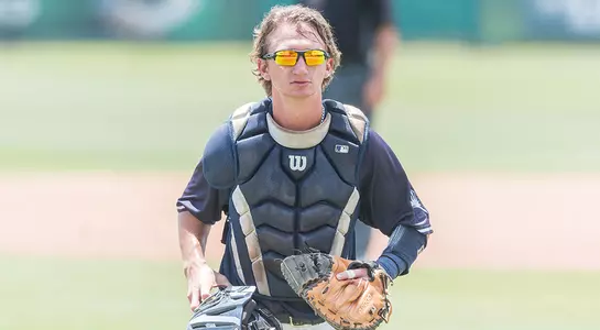Tanner Clark walks back to the plate with his catcher's gear on.