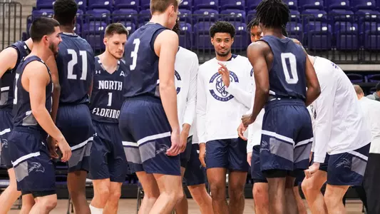 Basketball team stands in a huddle next to the court