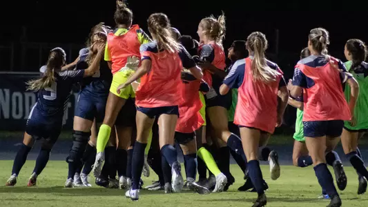 The women's soccer team holds a group huddle celebrating the game winning goal versus Lipscomb