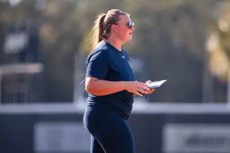 UNF Softball assistant coach walks onto field to talk to pitcher.
