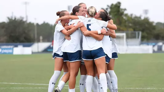 UNF Women's soccer team hugs and celebrates after scoring a goal.