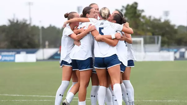 UNF Women's soccer team hugs and celebrates after scoring a goal.