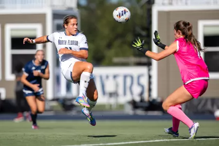 UNF Women's soccer player kicks the ball over opposing team's goalkeeper.