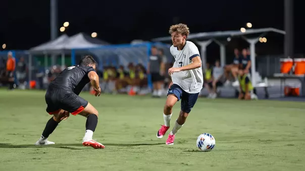 UNF Men's soccer player dribbles past a defender.