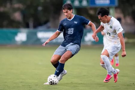 UNF Men's soccer player dribbles past a defender