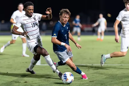 UNF men's soccer player dribbles the ball past a defender.