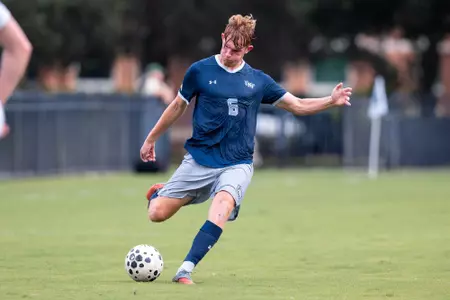 UNF men's soccer player kicks the ball.
