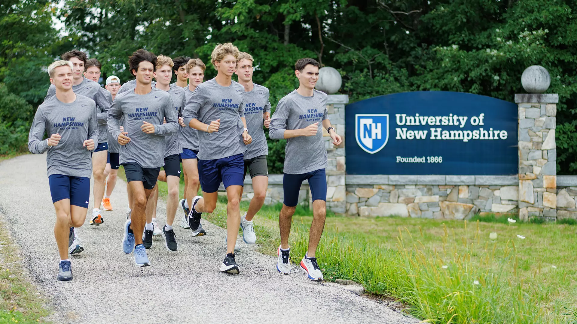Men's XC Team Runs on Main Street adjacent to Welcome to UNH sign