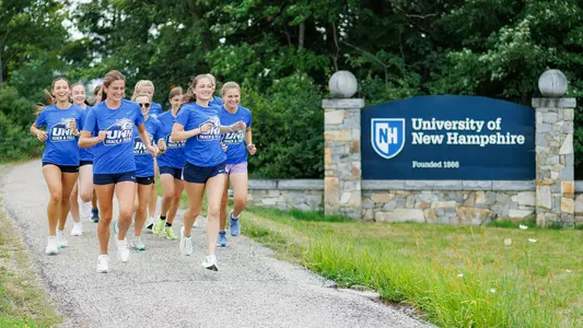 Women's XC Team Runs on Main Street adjacent to Welcome to UNH sign