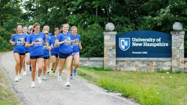Women's XC Team Runs on Main Street adjacent to Welcome to UNH sign