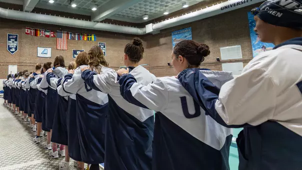 Members of swim team hold teammate shoulders while standing at attention for national anthem