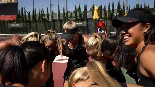 The USC Women's Tennis team huddles together on the court and smiles.