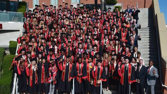 The 2018 graduating USC student-athletes stand on the steps outside of the Galen Center.
