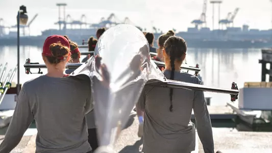 The USC women's rowing team walks their boat to the water.