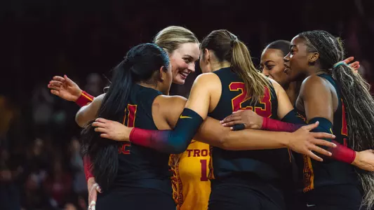 USC women's volleyball players gather in a circle with senior outside hitter Ally Batenhorsts' face visible from the side at the net during a match against Iowa, in which the Trojans won, 3-0.