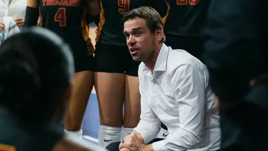 Tyler Hildebrand kneels down to coach the USC women's volleyball team during a timeout.