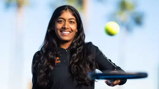 Krisha Mahendran holds a tennis racket out front with palm trees in background