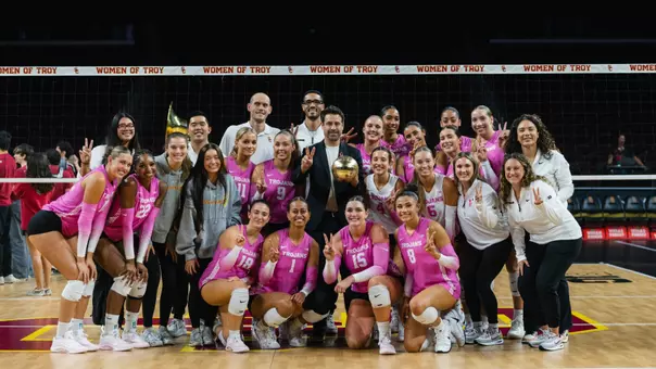 USC women's volleyball head coach Brad Keller poses with the team at center court in Galen Center to celebrate his 100th-career win