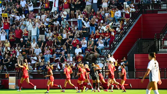 USC Soccer team celebrates a goal with fans in front of the stands at Rawlinson Stadium.