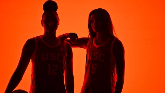 JuJu and Jazzy pose with a basketball in dim lighting.
