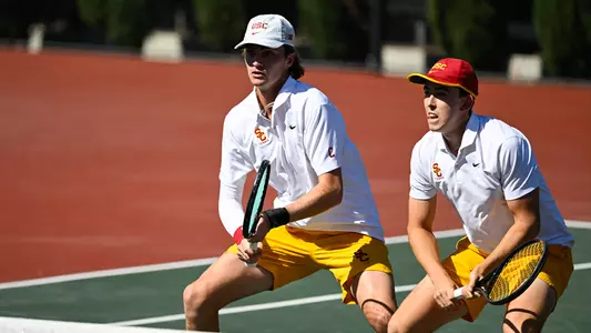 jack and andrin squat near net holding rackets