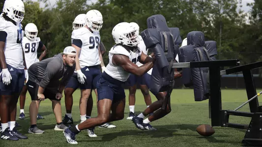 Jay Person hits the sled under the watchful eye of Coach Nick Davison.