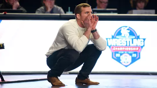 Coach Kyle Ruschell makes a call squatting on the mat during SoCon Championships