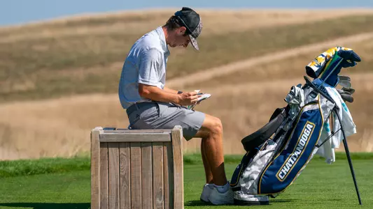 Braedon Wear looks over his yardage book taking a seat awaiting his next tee shot.