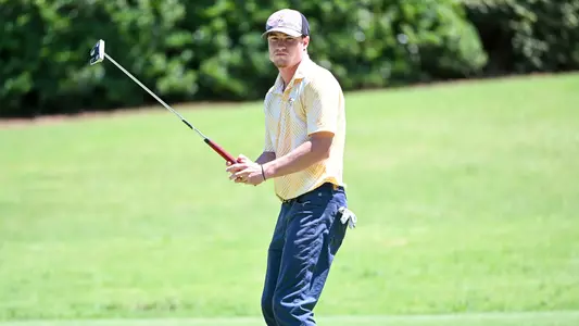 John Houk leans and lifts his putter as his putt approaches the hole