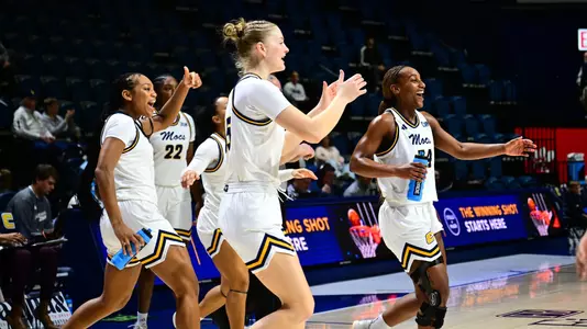 Several women's basketball players on the bench celebrating a teammates play.