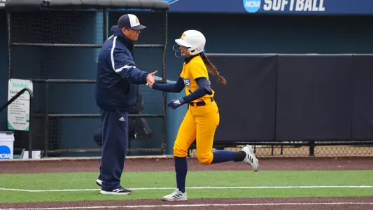softball player high-fiving coach and running toward home.