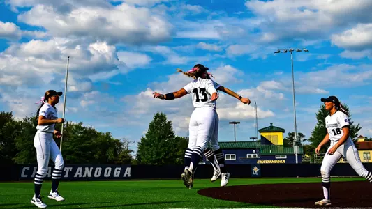 Two softball players jumping up in celebration with two watching