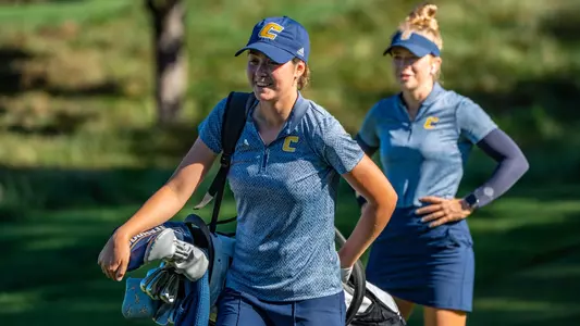 Chloe Stevenazzi with a grin as she puts her bag across her shoulder walking toward her next shot with coach Sarah Busy in the background.
