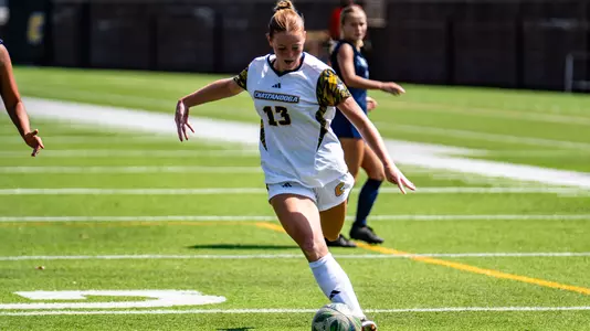 A soccer player in a white kit is kicking the ball on a sunny day.