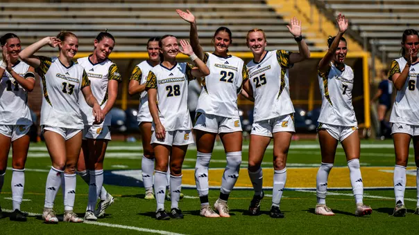 Soccer players in white are waving to the crowd after a win from the pitch.