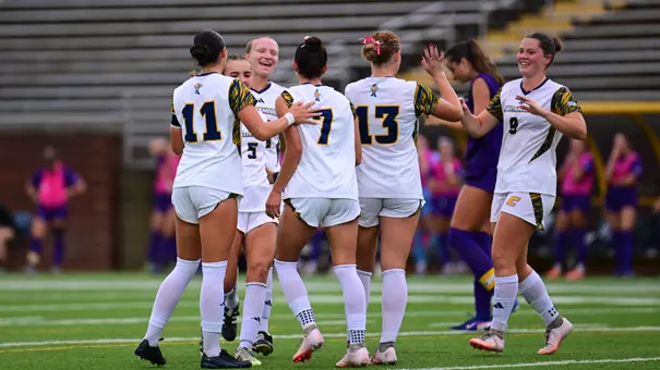 Several soccer players in white are celebrating a goal with high fives and back pats.