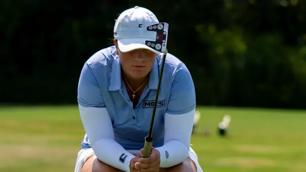 Bella Bugg is crouched down reading a putt on the green with her putter angled up to help with aim.