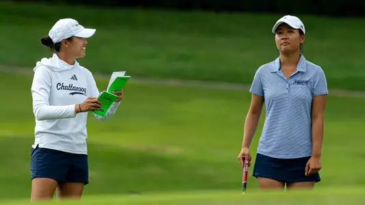 Assistant Coach Shelley Chen smiles as she shares course info as Elizabeth Jang surveys shot options in the fairway.