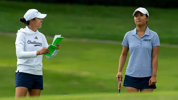 Assistant Coach Shelley Chen smiles as she shares course info as Elizabeth Jang surveys shot options in the fairway.