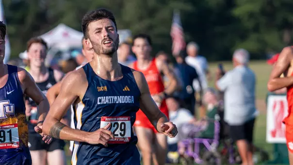 A cross country runner in blue is approaching the finish line in a race.