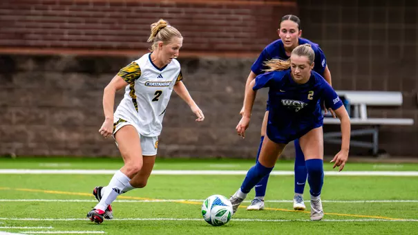 A soccer player in white is taking control of the ball against a defender in dark colors.