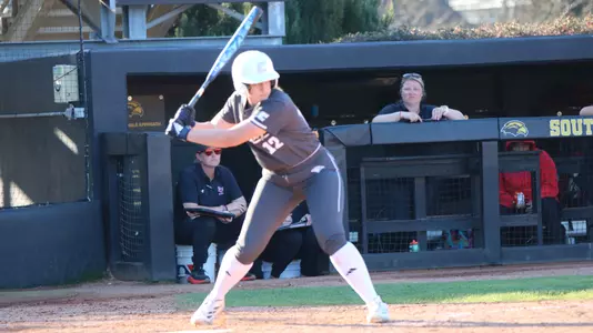 A softball player is at the plate waiting for the pitch.