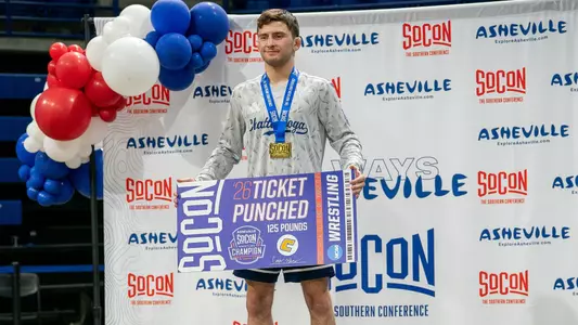 Cooper Flynn stands atop the SoCon podium holding his ticket poster that he punched to the 2026 NCAA Wrestling Championships