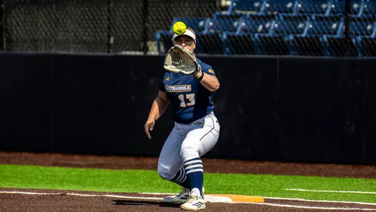 A softball player catches the ball at first base for an out.
