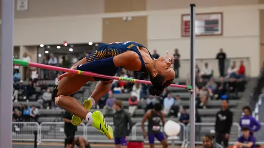 A woman field athlete is flopping over the high jump bar at a competition.