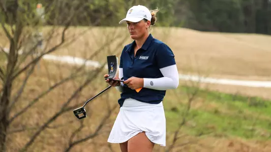 Bella Bugg checks her yardage book while holding her putter trying to read the green for her birdie effort