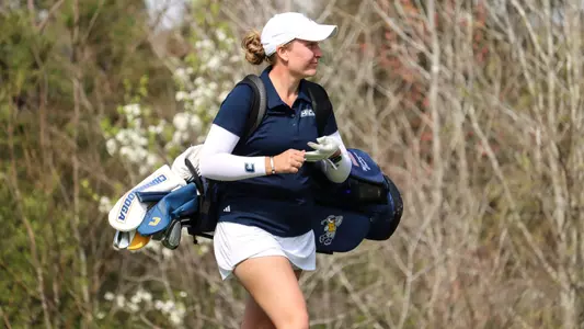 Makenzie Cooper walks towards the green with her bag and starts to take off her glove in preparation for a birdie putt