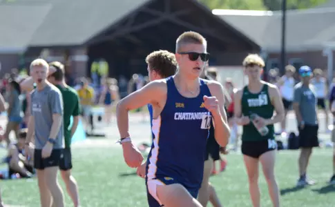 A male college athlete is running a race on a track on a sunny day.