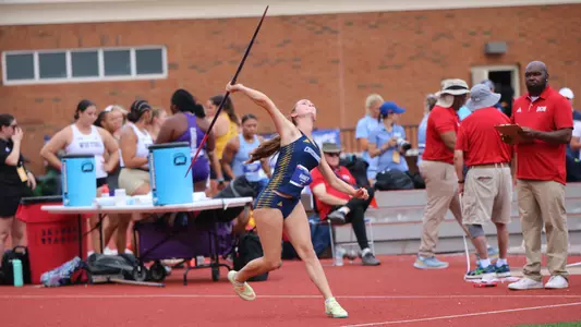 A track and field athlete is throwing a javelin while others look on.