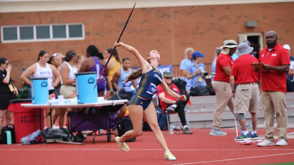 A track and field athlete is throwing a javelin while others look on.